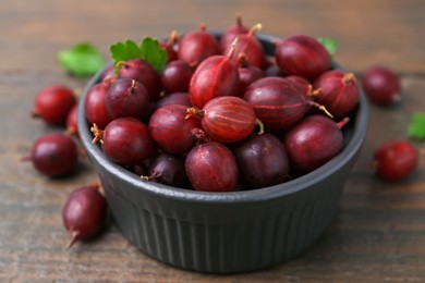Photo of Ripe red gooseberries in bowl on wooden table, closeup