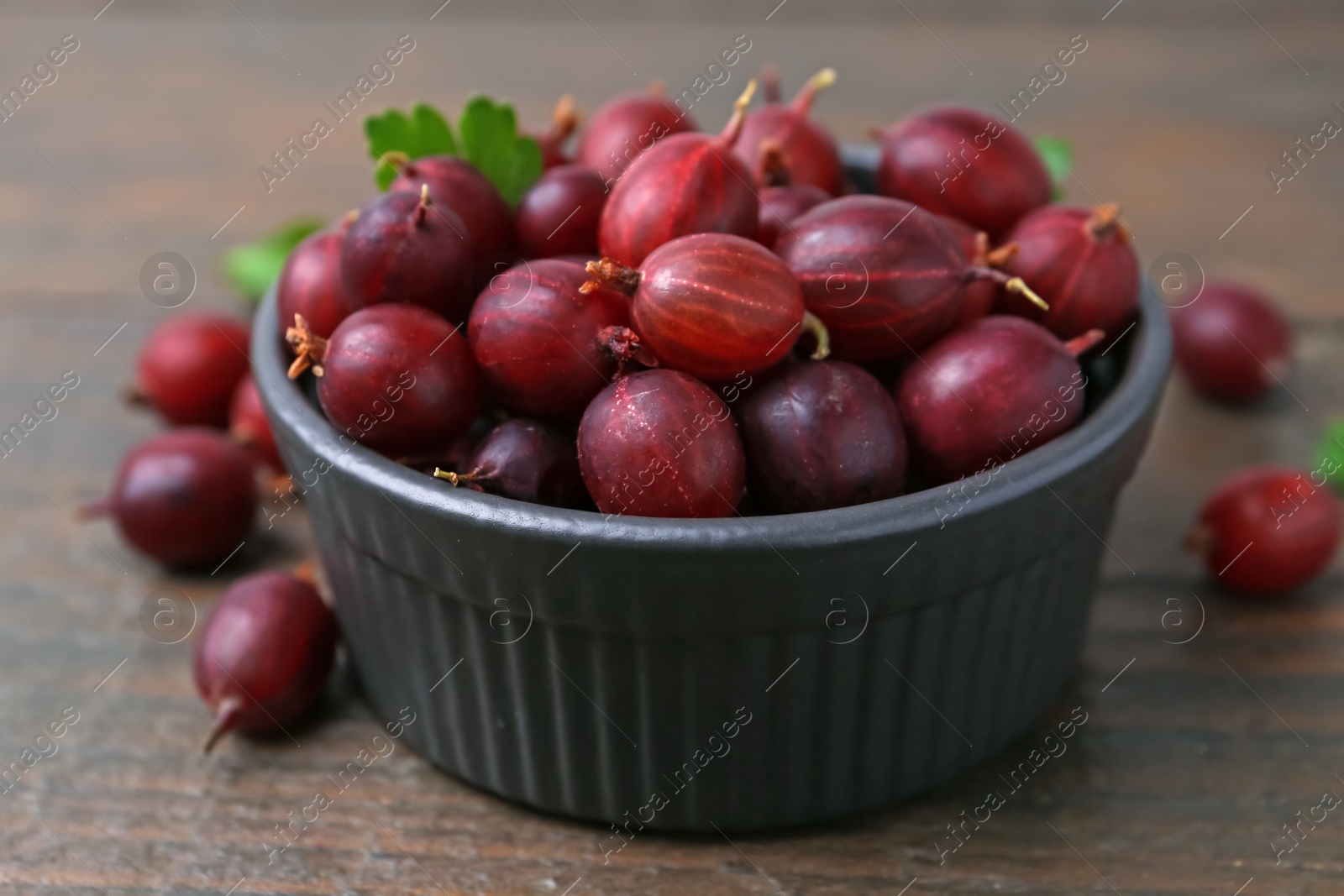 Ripe red gooseberries in bowl on wooden table, closeup Photo of Ripe red gooseberries in bowl on wooden table, closeup