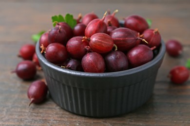 Photo of Ripe red gooseberries in bowl on wooden table, closeup