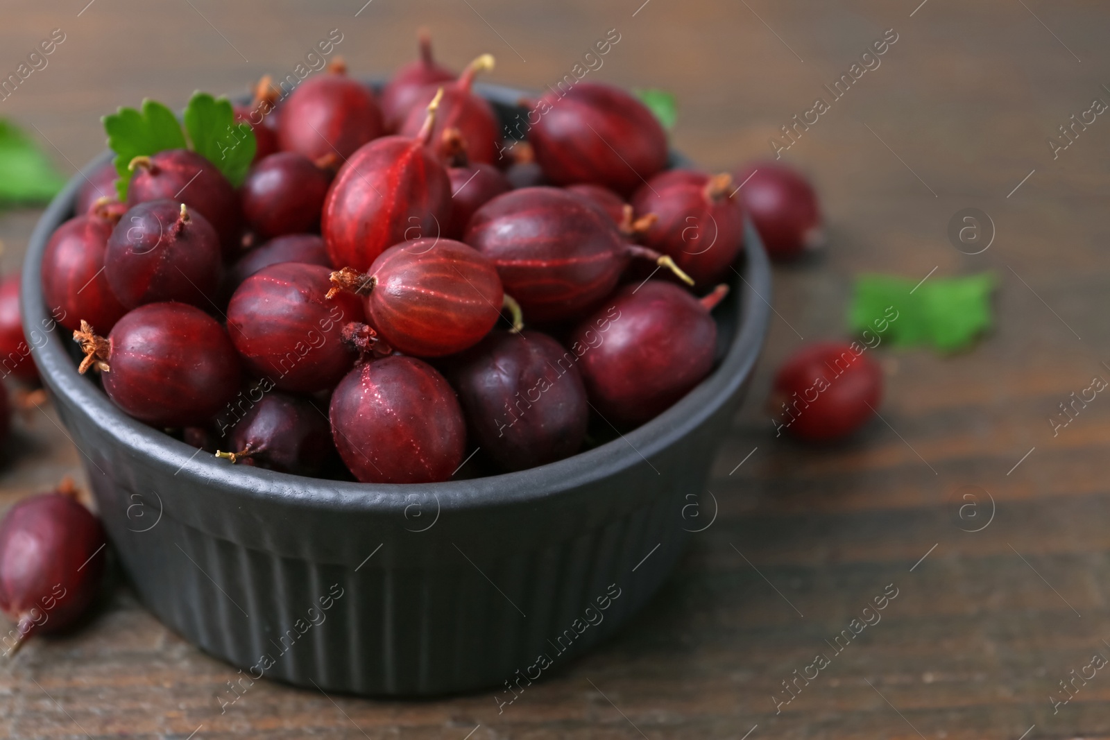 Ripe red gooseberries in bowl on wooden table, closeup Photo of Ripe red gooseberries in bowl on wooden table, closeup