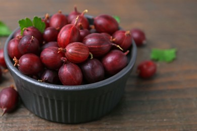 Photo of Ripe red gooseberries in bowl on wooden table, closeup