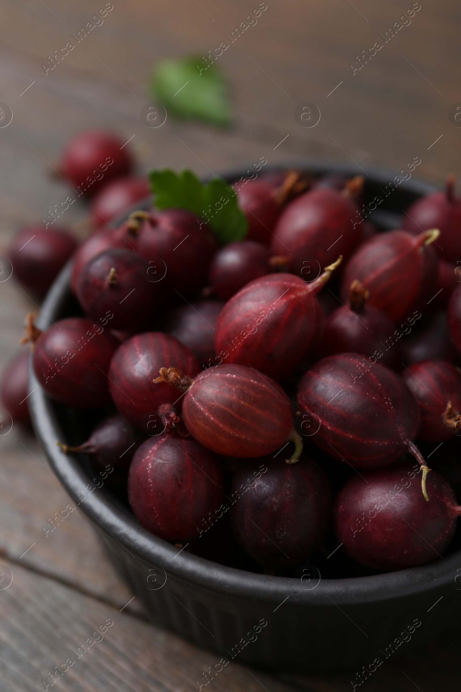 Ripe red gooseberries in bowl on wooden table, closeup Photo of Ripe red gooseberries in bowl on wooden table, closeup
