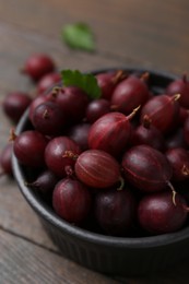 Photo of Ripe red gooseberries in bowl on wooden table, closeup