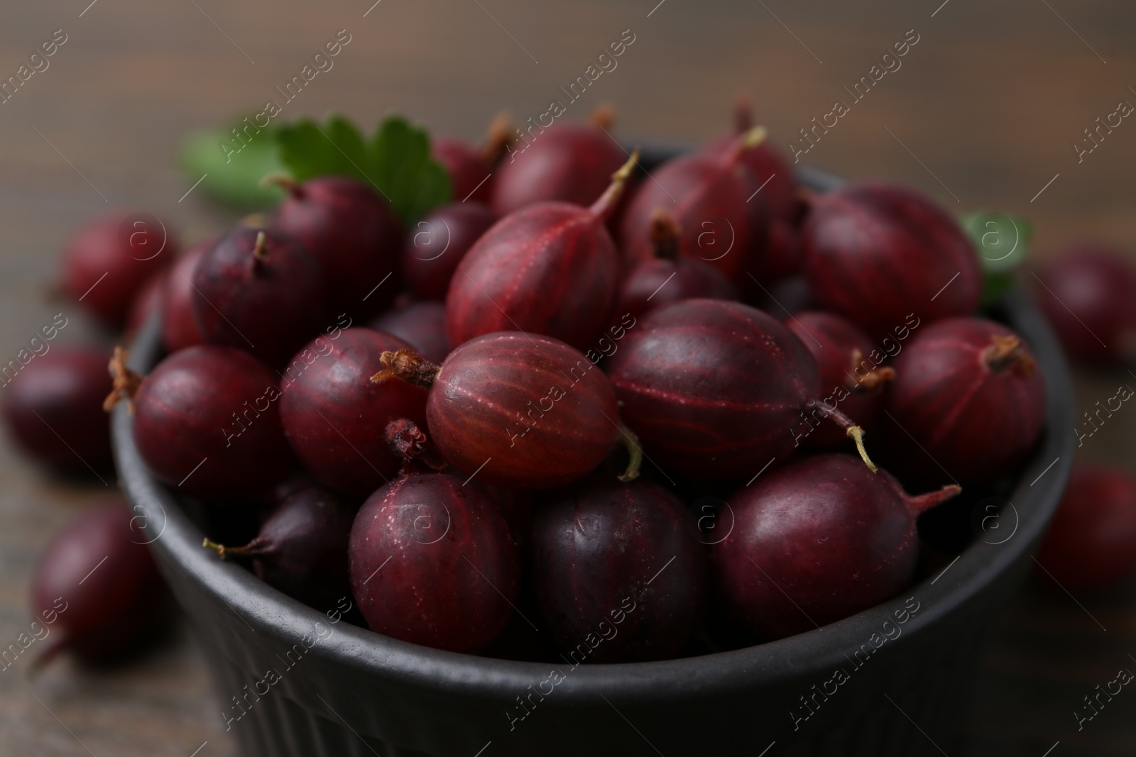Ripe red gooseberries in bowl on wooden table, closeup Photo of Ripe red gooseberries in bowl on wooden table, closeup
