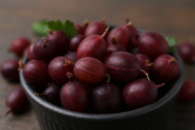 Photo of Ripe red gooseberries in bowl on wooden table, closeup