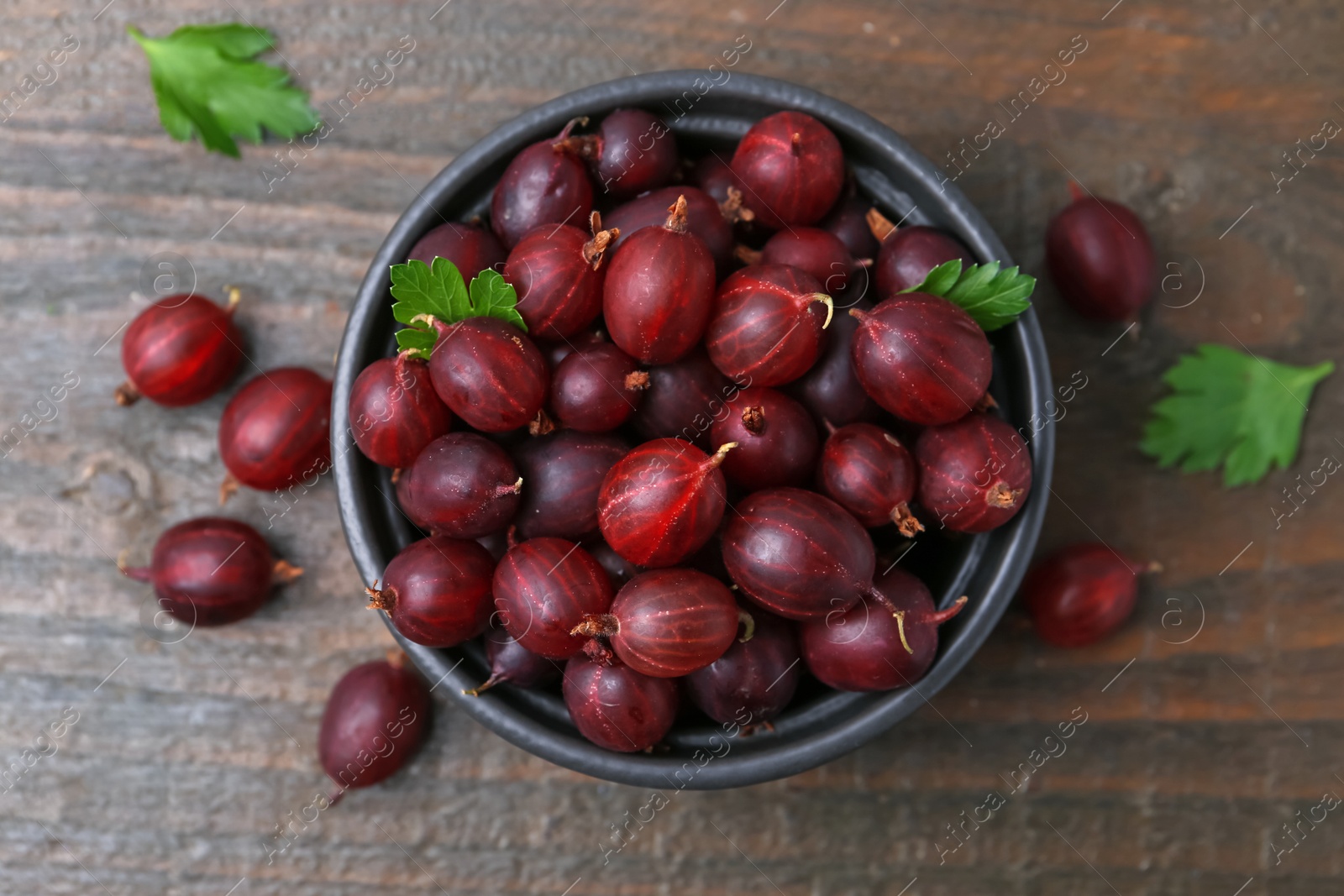 Ripe red gooseberries in bowl on wooden table, flat lay Photo of Ripe red gooseberries in bowl on wooden table, flat lay