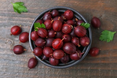 Photo of Ripe red gooseberries in bowl on wooden table, flat lay