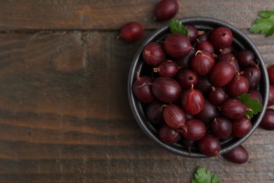 Photo of Ripe red gooseberries in bowl on wooden table, flat lay. Space for text