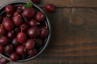 Photo of Ripe red gooseberries in bowl on wooden table, top view. Space for text