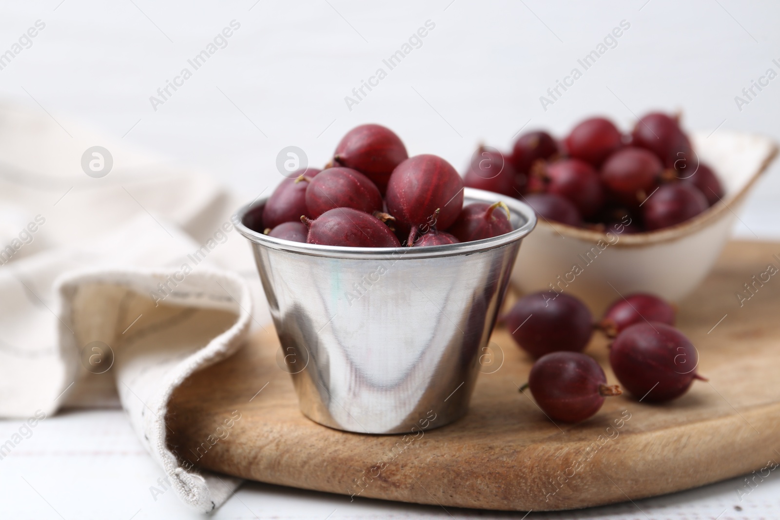 Ripe red gooseberries in bowl on white wooden table, closeup Photo of Ripe red gooseberries in bowl on white wooden table, closeup