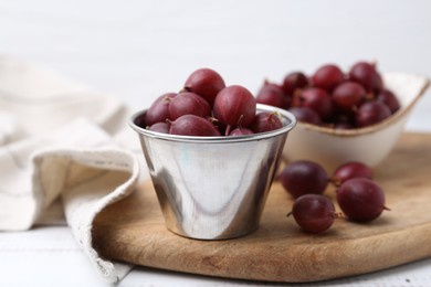 Photo of Ripe red gooseberries in bowl on white wooden table, closeup