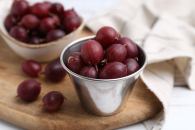 Photo of Ripe red gooseberries in bowl on white wooden table, closeup