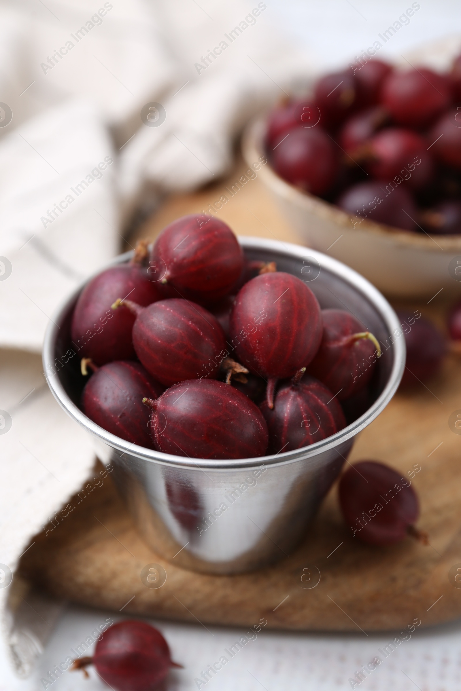 Ripe red gooseberries in bowl on white wooden table, closeup Photo of Ripe red gooseberries in bowl on white wooden table, closeup