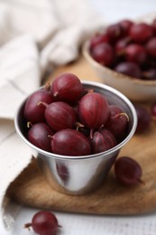 Photo of Ripe red gooseberries in bowl on white wooden table, closeup