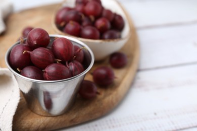 Photo of Ripe red gooseberries in bowl on white wooden table, closeup. Space for text