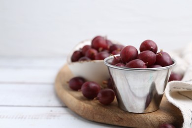 Photo of Ripe red gooseberries in bowl on white wooden table, closeup. Space for text