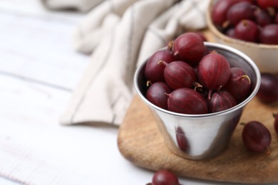 Photo of Ripe red gooseberries in bowl on white wooden table, closeup. Space for text