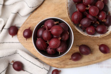 Photo of Ripe red gooseberries in bowl on white wooden table, flat lay