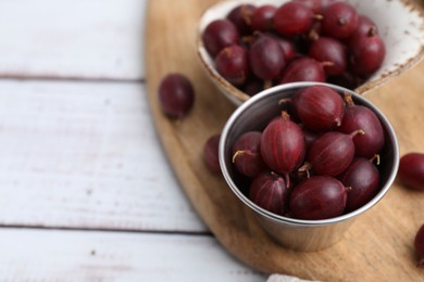 Photo of Ripe red gooseberries in bowl on white wooden table, closeup. Space for text