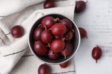 Photo of Ripe red gooseberries in bowl on white wooden table, flat lay