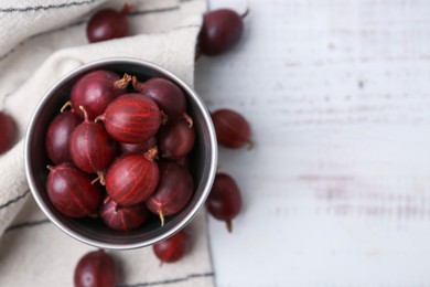 Photo of Ripe red gooseberries in bowl on white wooden table, flat lay. Space for text