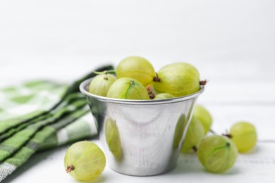 Photo of Ripe green gooseberries in bowl on white wooden table, closeup