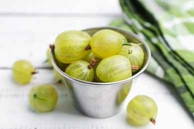 Photo of Ripe green gooseberries in bowl on white wooden table, closeup