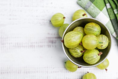 Photo of Ripe green gooseberries in bowl on white wooden table, flat lay. Space for text