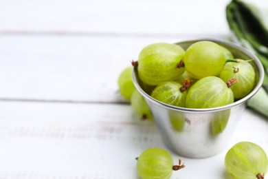 Photo of Ripe green gooseberries in bowl on white wooden table, closeup. Space for text