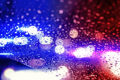 Image of Police red and blue lights at night, blurred view through wet glass. Bokeh effect