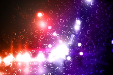 Image of Police red and blue lights in city at night, blurred view through wet glass