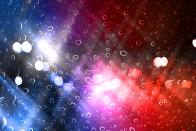 Image of Police red and blue lights in city at night, blurred view through wet glass