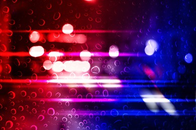 Image of Police red and blue lights in city at night, blurred view through wet glass