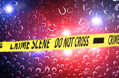 Image of Police yellow Crime Scene Do Not Cross tape. Red and blue lights, blurred view through wet glass