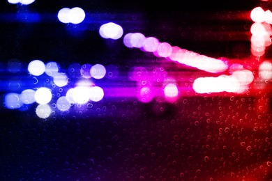 Image of Police red and blue lights in city at night, blurred view through wet glass