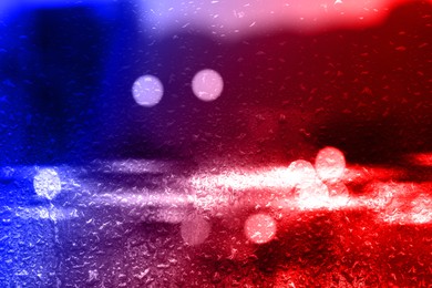 Image of Police red and blue lights in city, blurred view through wet glass