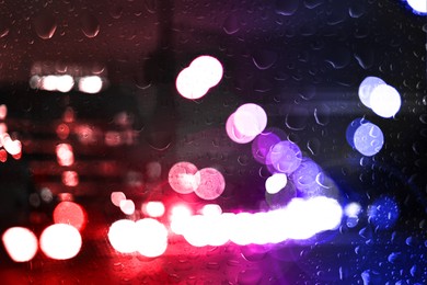 Image of Police red and blue lights in city at night, blurred view through wet glass