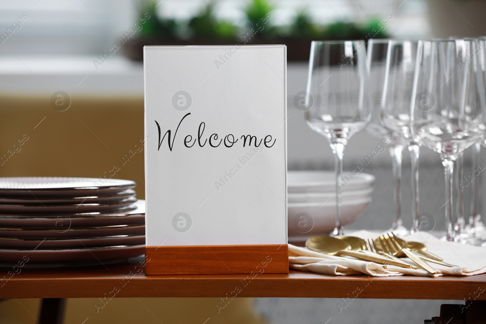 Image of Holder with word Welcome, clean dishware and cutlery on wooden table in restaurant