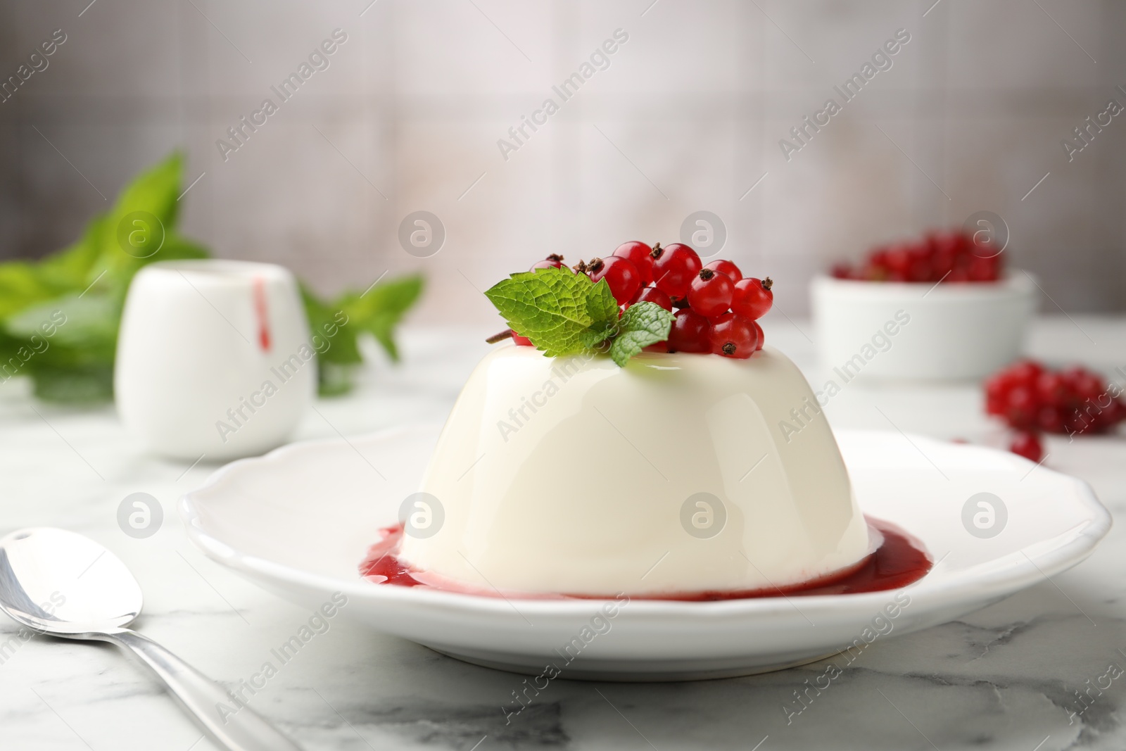 Photo of Delicious panna cotta with red currants, sauce and mint on white marble table against blurred background, closeup