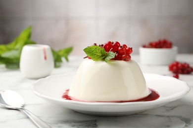 Photo of Delicious panna cotta with red currants, sauce and mint on white marble table against blurred background, closeup