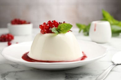 Photo of Delicious panna cotta with red currants, sauce and mint on white marble table against blurred background, closeup