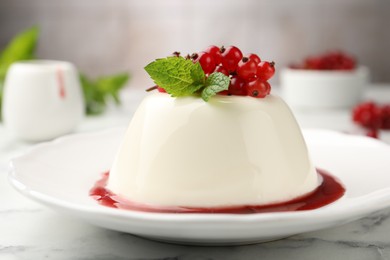 Photo of Delicious panna cotta with red currants, sauce and mint on white marble table against blurred background, closeup