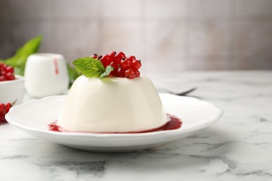 Photo of Delicious panna cotta with red currants, sauce and mint on white marble table against blurred background, closeup