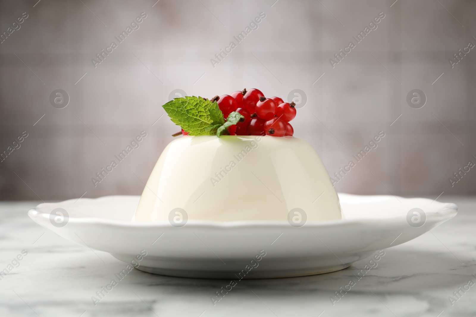 Photo of Delicious panna cotta with red currants, sauce and mint on white marble table against blurred background, closeup