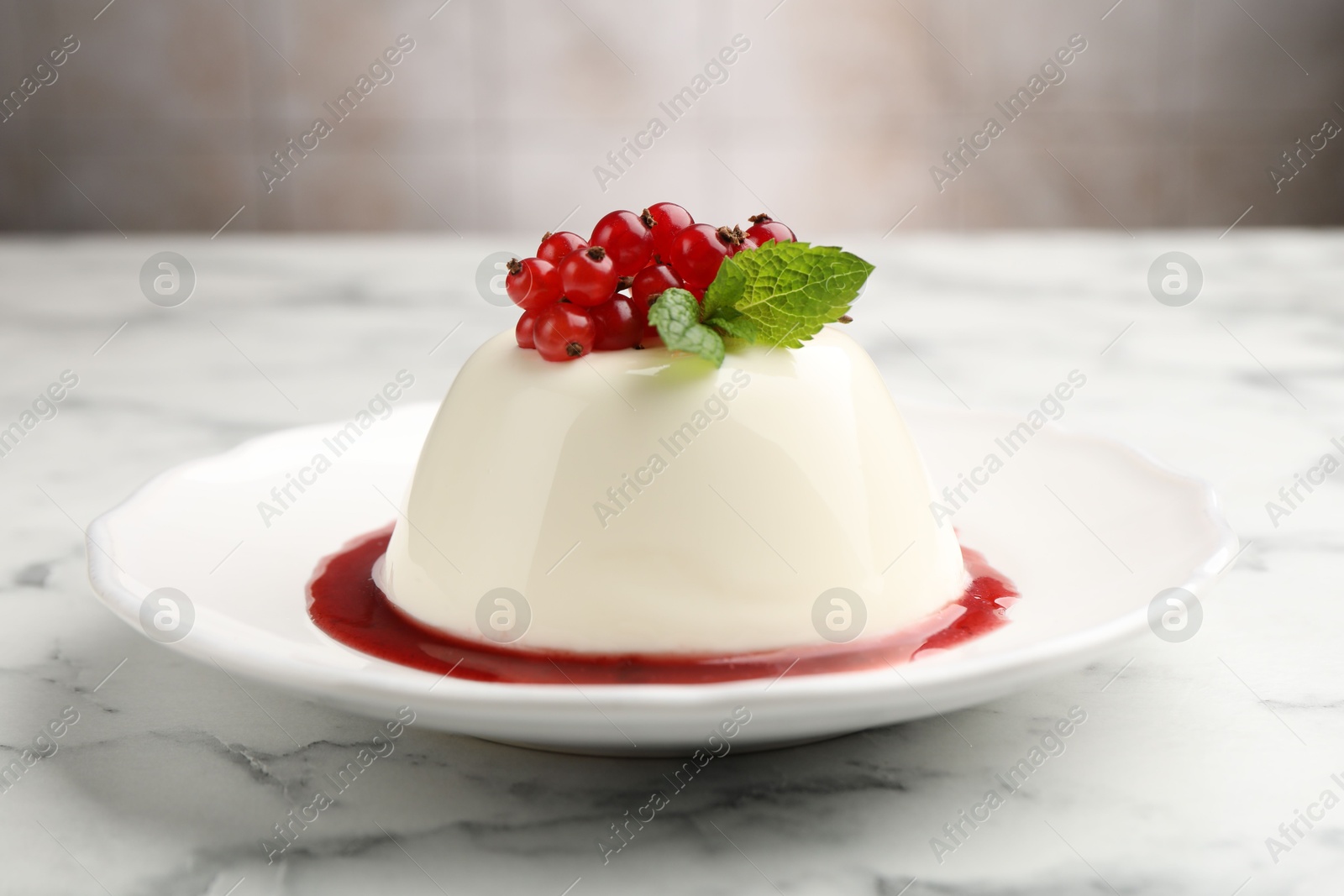 Photo of Delicious panna cotta with red currants, sauce and mint on white marble table against blurred background, closeup