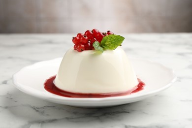 Photo of Delicious panna cotta with red currants, sauce and mint on white marble table against blurred background, closeup