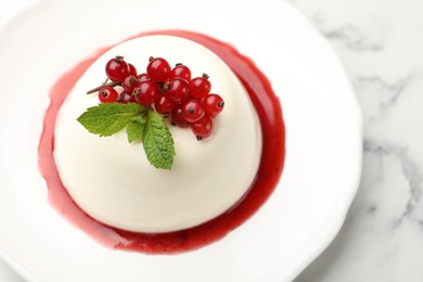 Photo of Delicious panna cotta with red currants, sauce and mint on white marble table, closeup