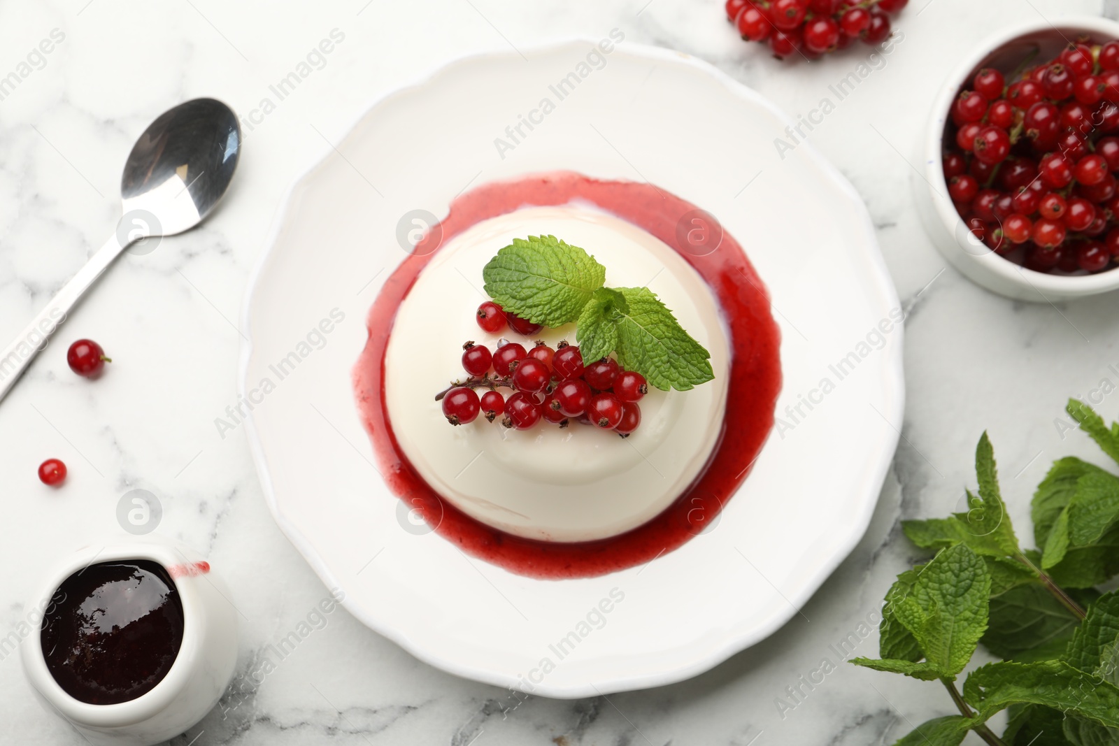Photo of Delicious panna cotta with red currants, sauce and mint on white marble table, flat lay
