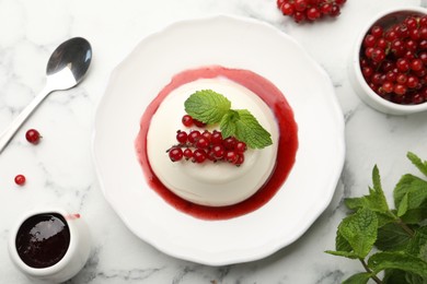 Photo of Delicious panna cotta with red currants, sauce and mint on white marble table, flat lay