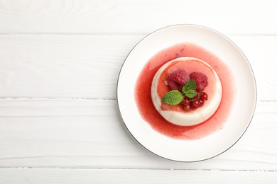 Photo of Delicious panna cotta with berries, sauce and mint on white wooden table, top view. Space for text